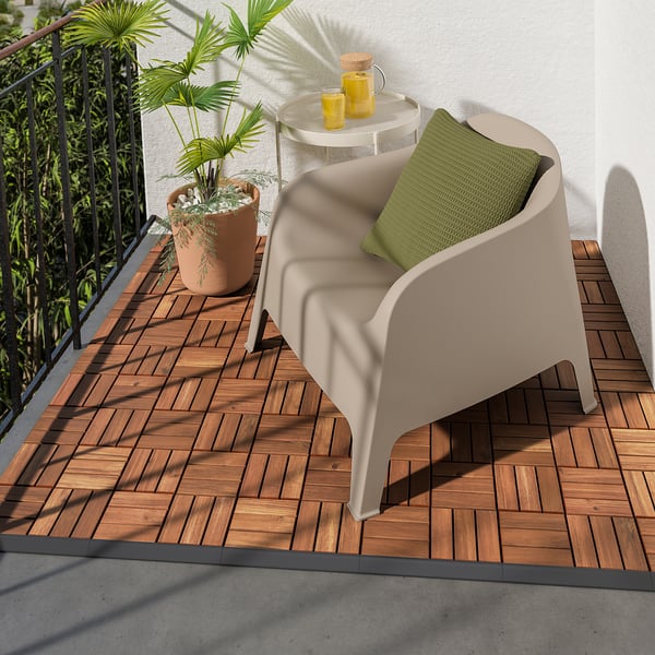 Balcon confortabil cu scaun bej RUNNEN, pernă verde, masă rotundă mică, două băuturi galbene și plante mari în ghiveci pe terasa din lemn.