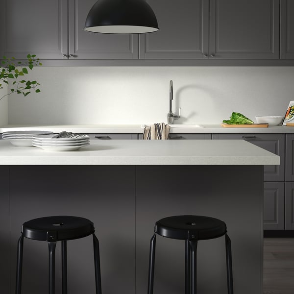 Bucătărie modernă minimalistă cu blat gri SÄLJAN, scaune de bar negre, farfurii, tacâmuri și lampă. Design curat și elegant.