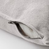 Prim-plan al pernei din material textil cu fermoar deschis pe husa texturată gri și albă.