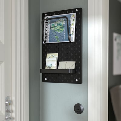 Placă perforată neagră SKÅDIS pe ușă, afișând obiecte în buzunare și raft.