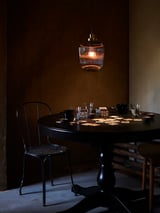 Cameră confortabilă slab luminată, cu masă rotundă întunecată, scaune, lampă suspendată din alamă și sticlă, configurație de băuturi.