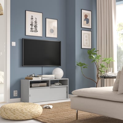 Living modern cu pereți albaștri, suport TV SPIKSMED alb, mobilier funcțional și decor.