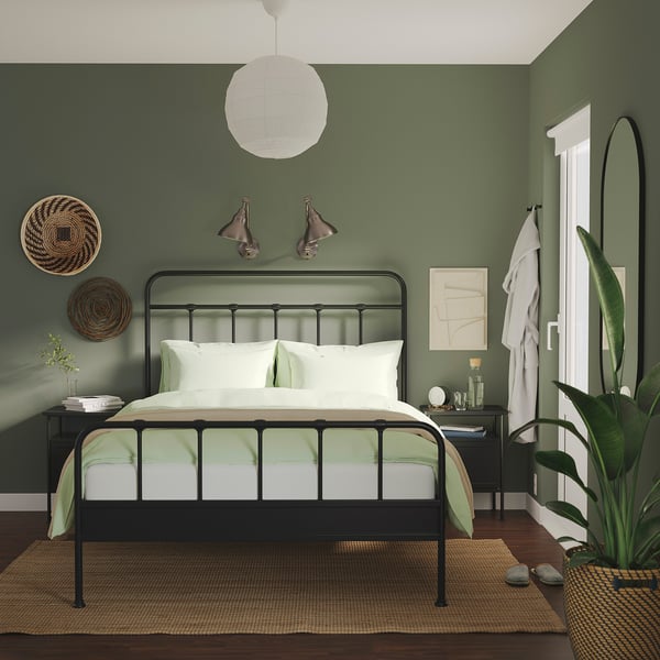 Dormitor modern verde închis cu pat negru, lenjerie de pat alb/verde și decor simplu.