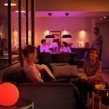 Două femei pe canapea, una cu băutură, cealaltă zâmbind. Zona barului în fundal, iluminare moale TRÅDFRI.