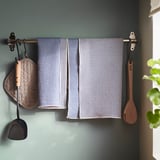 Suport de perete cu prosoape de bucătărie agățate, mănușă de bucătărie și ustensile din lemn.