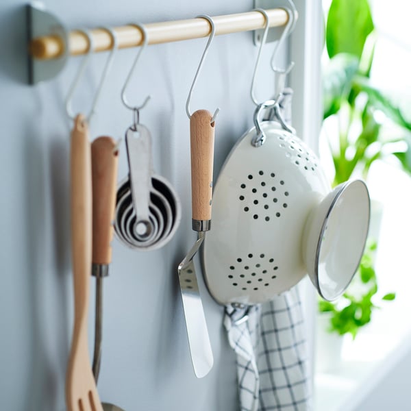 Ustensilele de bucătărie atârnă bine pe cârligele de perete. Include lingură cu fante, spatule și căni de măsurare. Spatula are mâner din lemn și gaură de agățat.