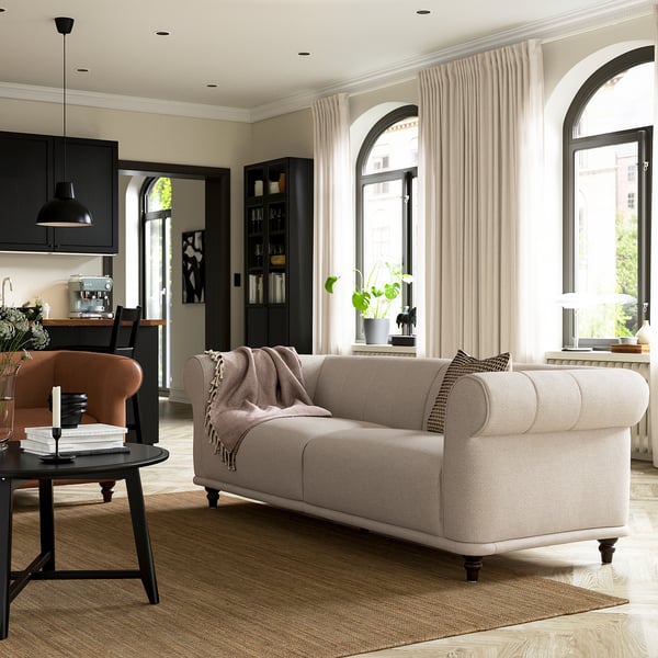 Living modern cu canapea bej deschis VISKAFORS, ferestre arcuite, mobilier negru și lumină naturală.