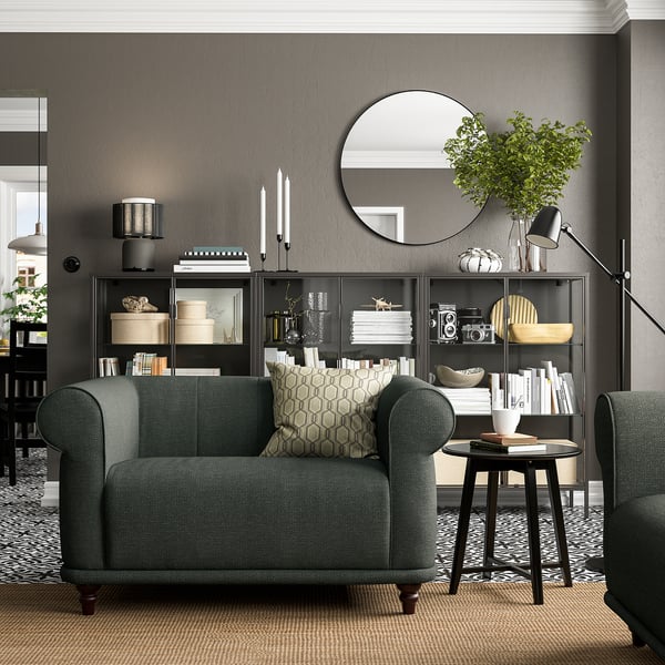 Living elegant cu fotolii din țesătură verde VISKAFORS, covor cu model, raft cu decor și lampă de podea, creând un spațiu confortabil și elegant.