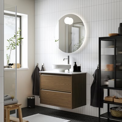 Modern bathroom with ÄNGSJÖN oak wash-stand, round mirror, white sink, wall-mounted cabinet for storage.