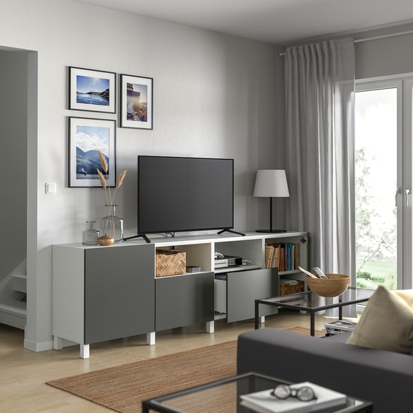 Modern living room with BESTÅ grey tv unit, flat screen tv, decorative frames, lamp, and a dark grey sofa near a large window with curtains.