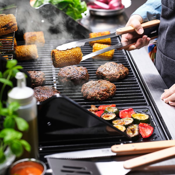 Grilling corn, burgers, courgette, bell peppers on gas grill.