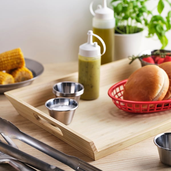 Wooden serving board with handles, small metal cups, corn, burgers in basket, herbs, tongs. GRILLTIDER product.