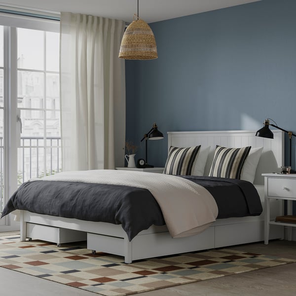 Modern white bed with drawers, rug, lamp.