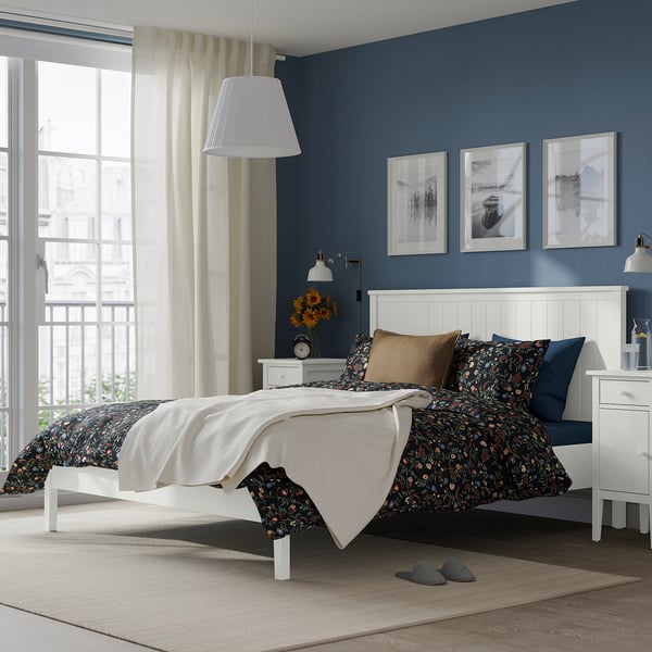 Cosy bedroom with white GULLABERG bed, floral duvet, pendant lamp, sunflowers, and city view.