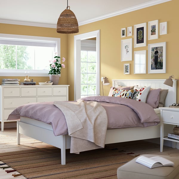 Bedroom with white GULLABERG bed, drawers, and bedside table. Light purple bedding, colourful pillows. Natural light and hanging lamp.