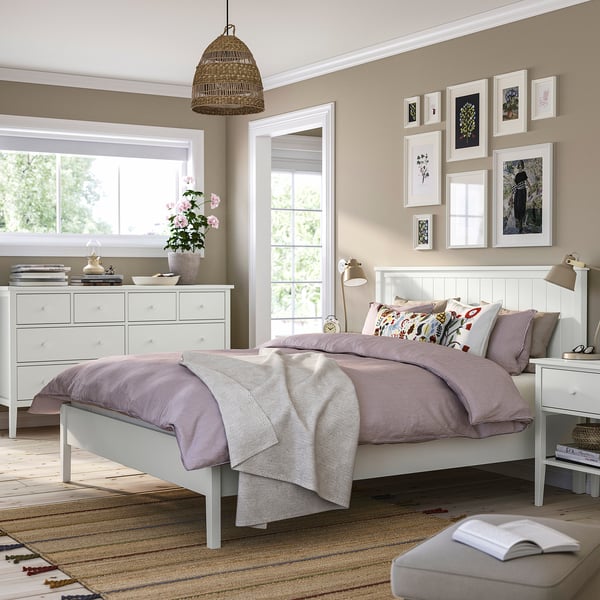 GULLABERG bed in purple & white linens, beside a window & plant-topped chest.