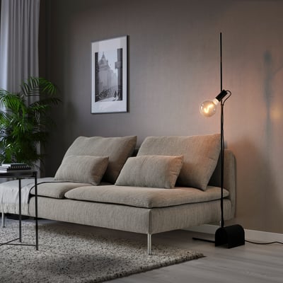 A modern living room with a grey HÅRSLINGA floor lamp and a sofa. The lamps light is warm and adjustable, enhancing the cosy atmosphere.