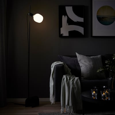 Modern living room with HÅRSLINGA floor lamp lighting grey couch, warm light, abstract art, candles.