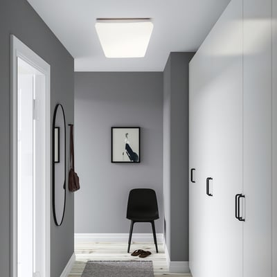 Modern entryway with a black chair, round mirror, and white cabinet; a square ceiling light.