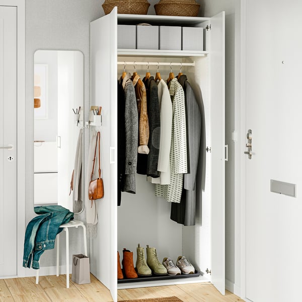 Closed wardrobe with hanging clothes, shoes below, mirror left, small seat with jacket.