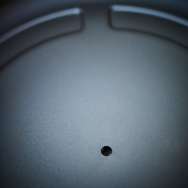 Close-up view of a dark grey metal outdoor plant pot with a draining hole and rounded handles.