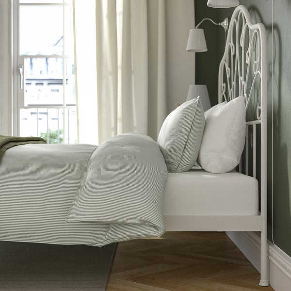 A white metal bed with a high headboard and striped bedding, situated near a large window with curtains, providing a cosy, well-lit space.