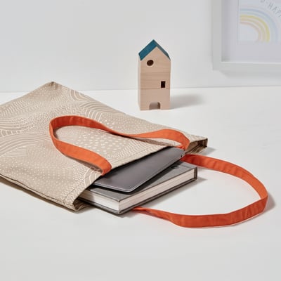 Beige tote bag with orange handles, white pattern, for laptop & papers.