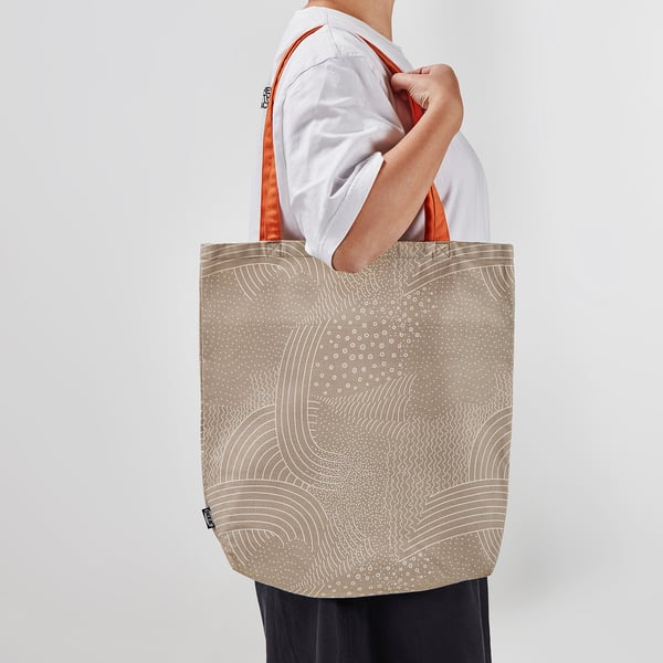 Person holding large beige tote bag with orange handles and white circular patterns.
