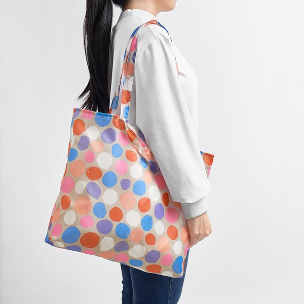 Person carrying a brightly coloured polka dot tote bag over the person shoulder. The bag is lightweight and can be folded into its own pocket.