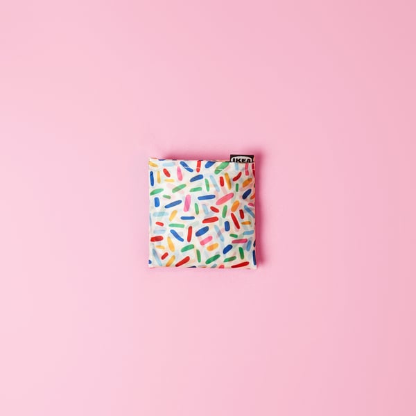 Square bag, colourful patterns on light backdrop, IKEA label, folds into pocket, versatile carry.