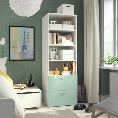 A SMÅSTAD bookcase in mint green with various storage items. Bright and compact, it fits well next to a bed with a map poster behind.
