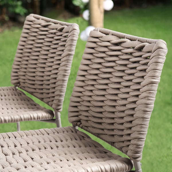 Beige wicker chairs with metal frames outdoors. Stackable and durable for outdoor use.