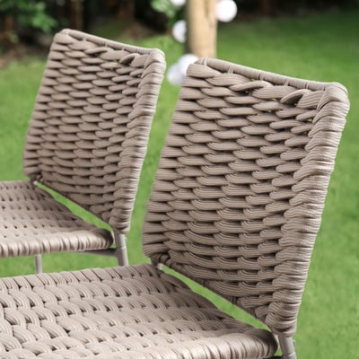 Beige wicker chairs with metal frames outdoors. Stackable and durable for outdoor use.