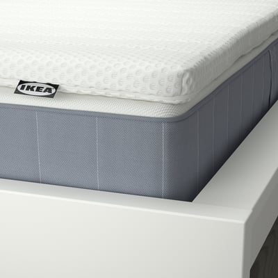 A grey VESTERÖY pocket spring mattress with a removable soft white top layer. Square-shaped, it offers a firm sleep surface for back sleepers.