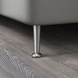 A close-up of a stainless steel furniture leg on a dark wooden floor.
