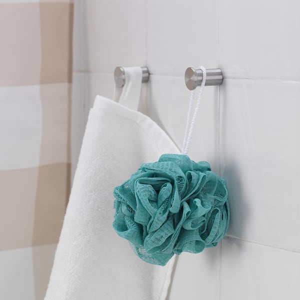Turquoise mesh body puff hangs in bathroom next to white towel.