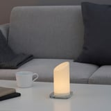 A modern living room a grey sofa with a lit led candle on a white table, emitting warm light.