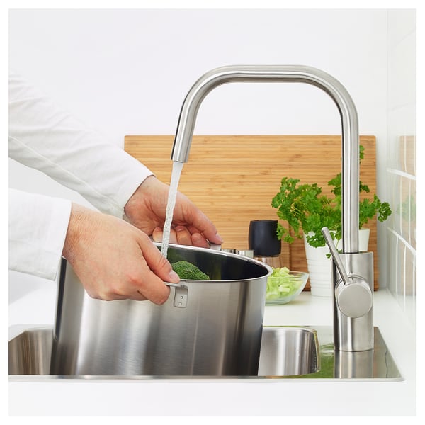 Person washes vegetables in sink with ÄLMAREN stainless steel tap, conserving water and energy.