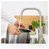 Person washes vegetables in sink with ÄLMAREN stainless steel tap, conserving water and energy.