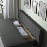 Modern grey sofa with hidden bed, white pillows, wall art, and plant.