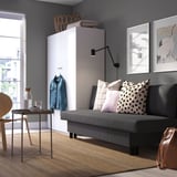 Modern living room with gray sofa-bed, white cabinet, wooden table, and wall art. Colorful pillows on sofa.