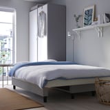 Modern sofa-bed in bedroom with storage, neatly arranged bedding, wall shelves, and city view.