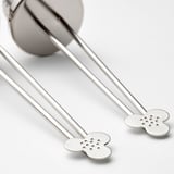 Silver tea infuser with long handles and round perforated ends sits on a table.