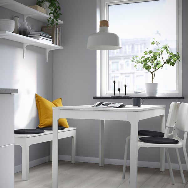 Modern dining area with white table, black cushions, large window, and decorative shelves.