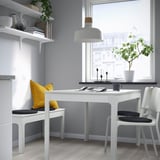 Modern dining area with white table, black cushions, large window, and decorative shelves.