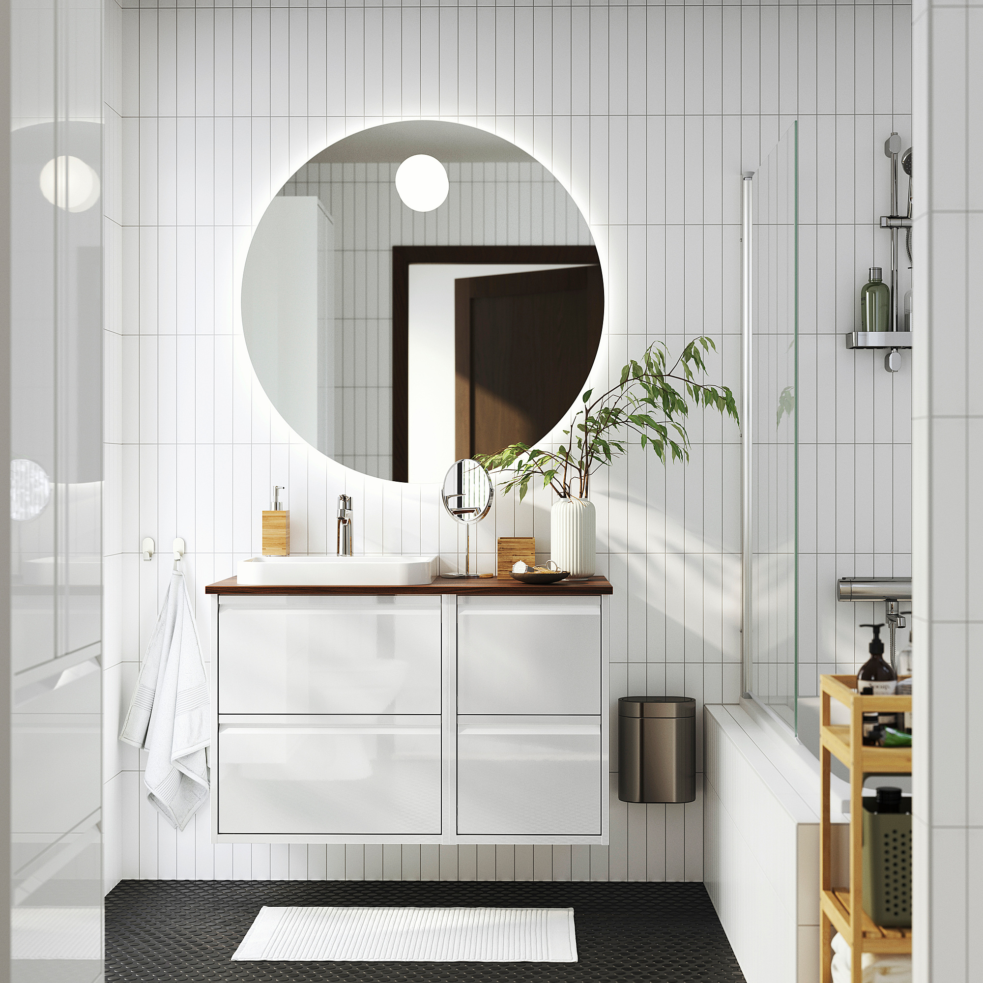 Modern white bathroom with round mirror, sleek vanity, and glass shower. White towels and plants decorate.