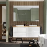 Modern bathroom vanity with dual sinks, striped wall, large mirror, glass shower, hanging towels, and a white tub. A rug and stool are on the floor.