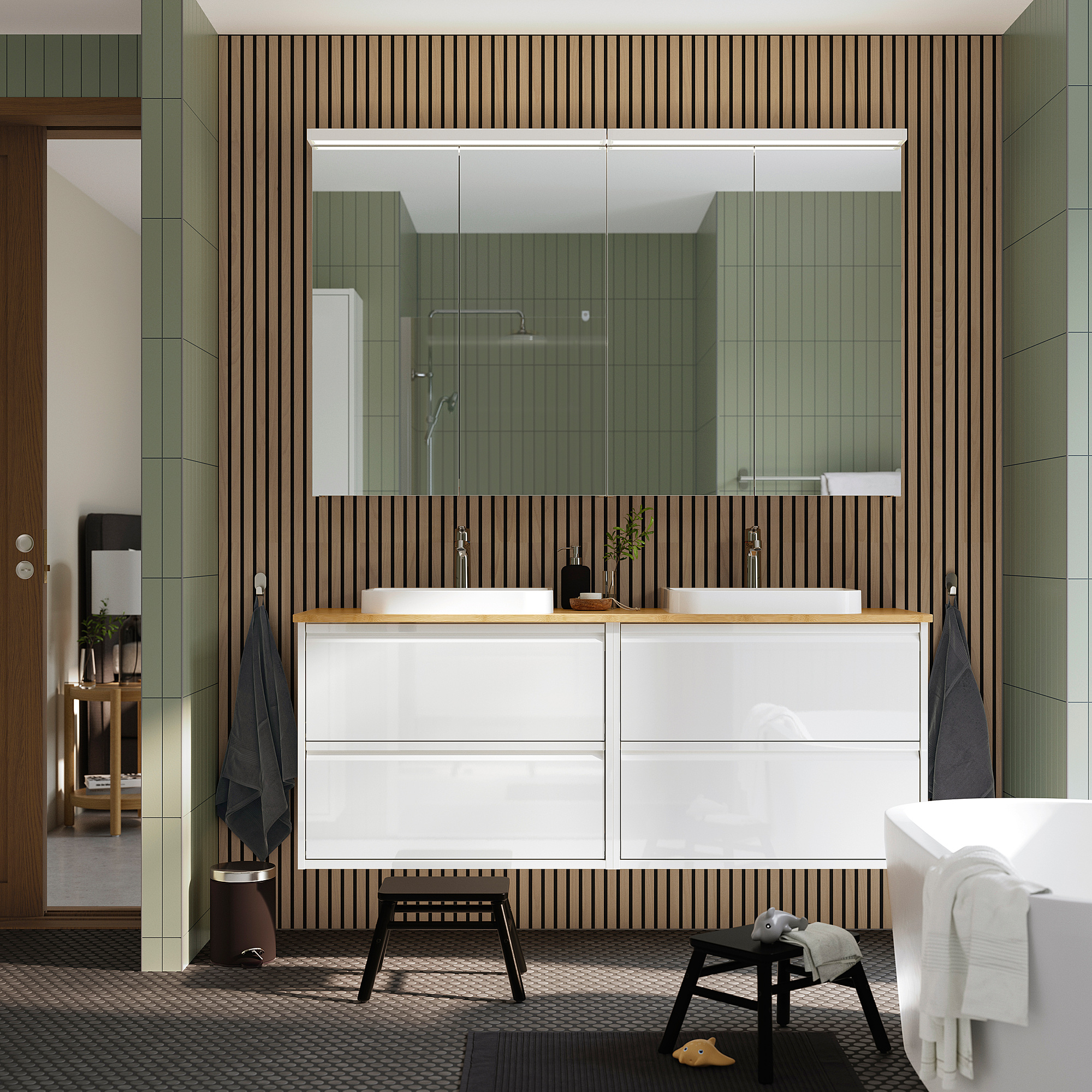 Modern bathroom vanity with dual sinks, striped wall, large mirror, glass shower, hanging towels, and a white tub. A rug and stool are on the floor.