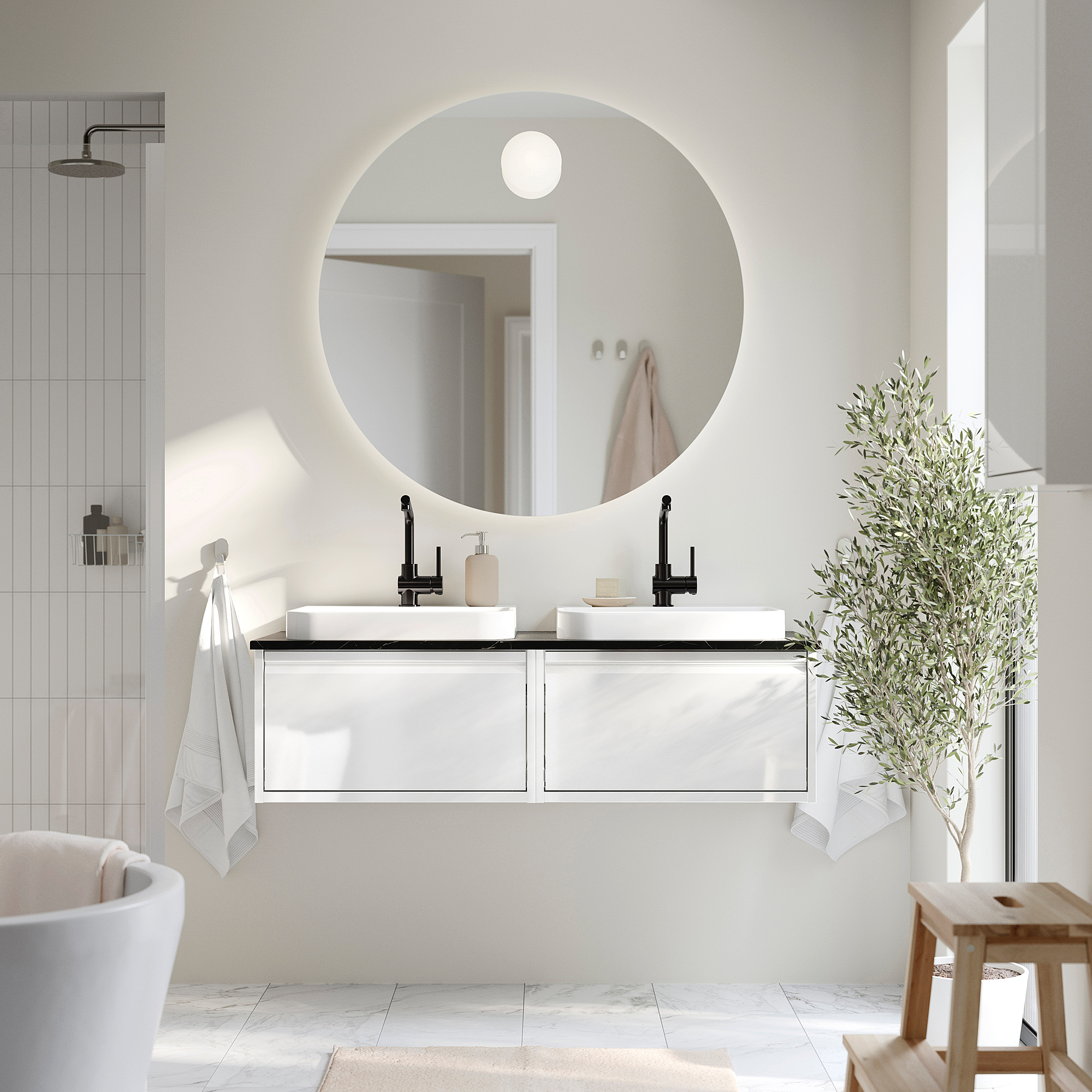 Modern white bathroom with floating double sink vanity. Round mirror and olive plant. Black fixtures.