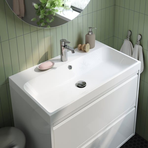 Modern white bathroom vanity with sleek sink, drawer, and chrome faucet against green tiled wall with mirror.